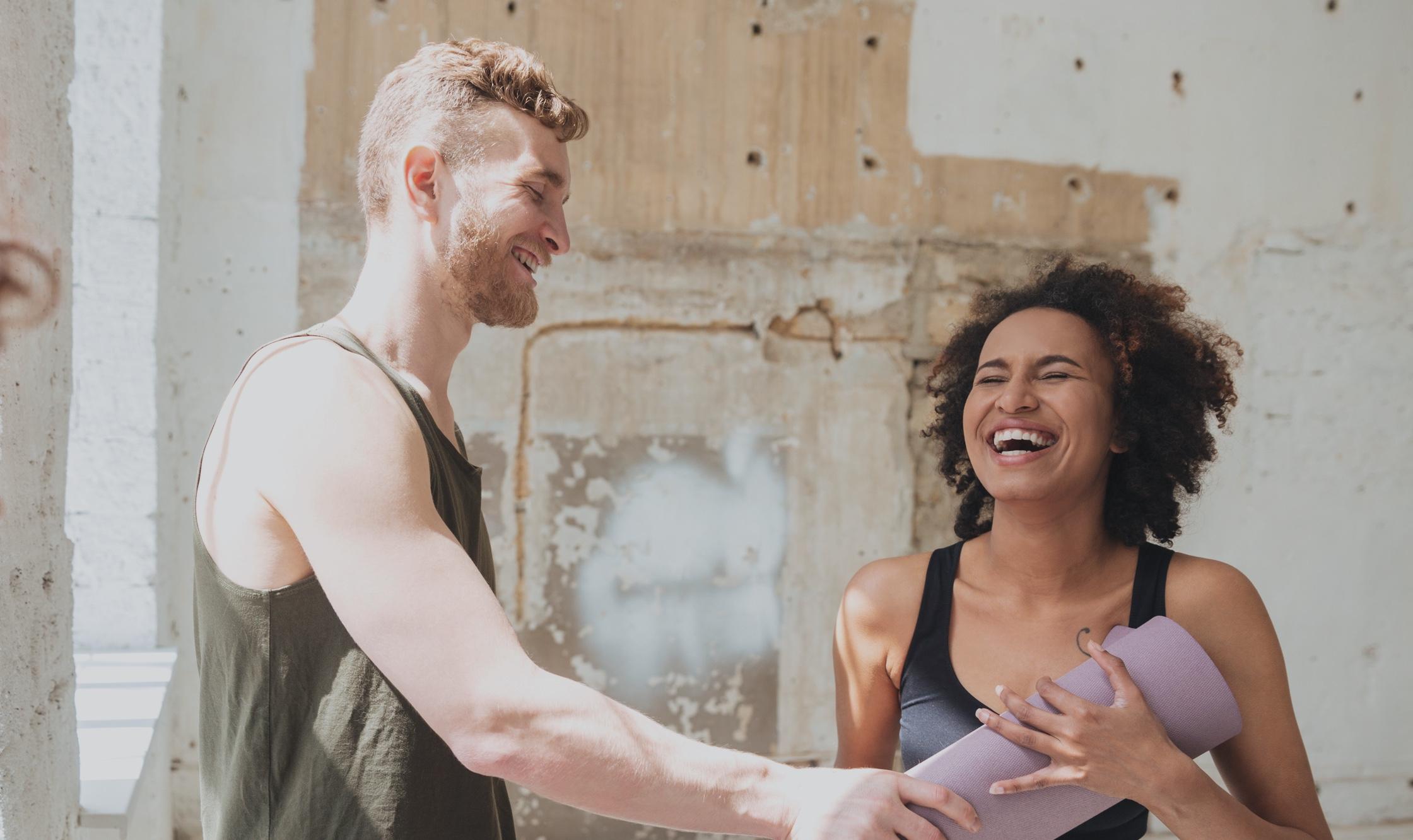 A laughing man and woman exchanging a yoga mat