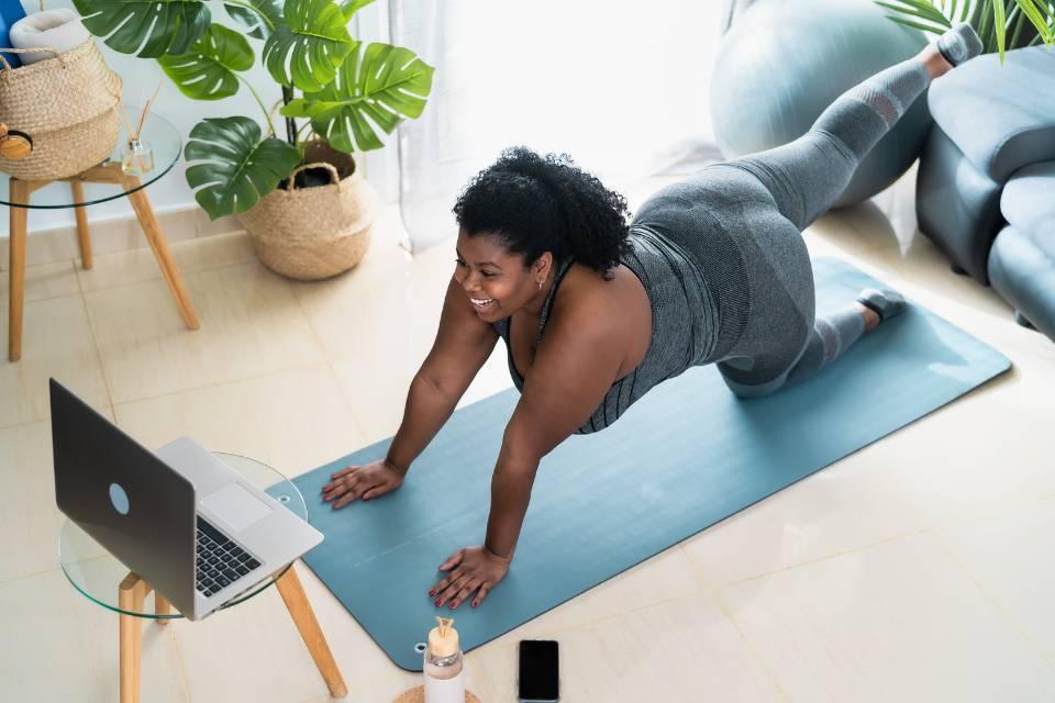 A smiling woman doing pilates in front of her laptop