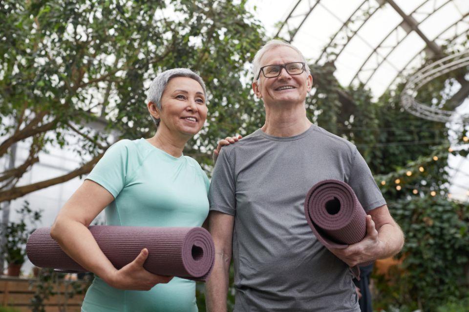 A smiling couple of seniors standing with rolled up yoga mats