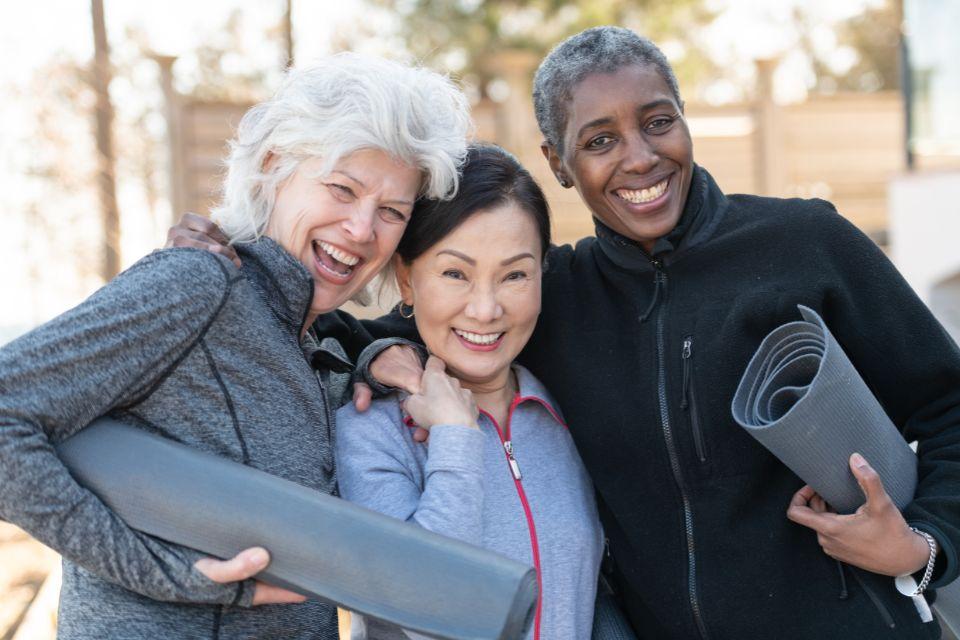 Three smiling women standing together with rolled up yoga mats