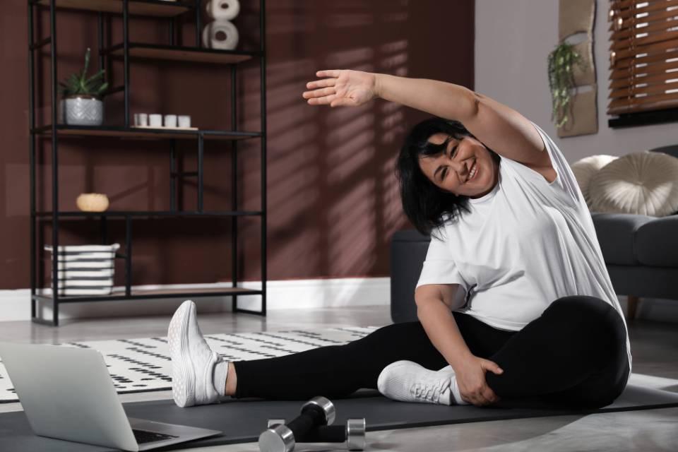 A smiling woman stretching on the floor in front of her laptop