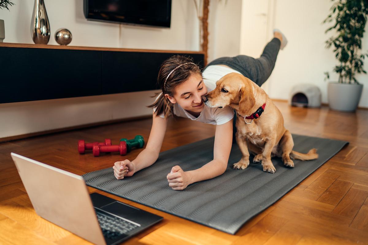 A person holding a one-legged plank while their dog says hi