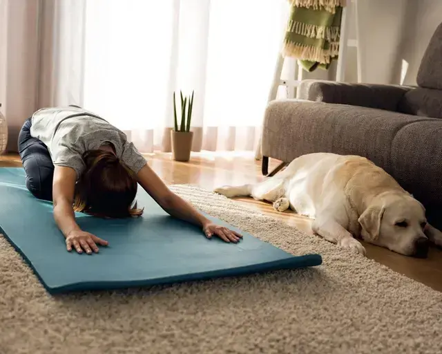 woman on a yoga mat doing childs pose with dog next