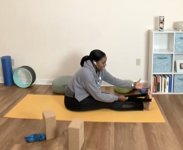 Chanel Sledge, smiling in a meditation pose with prayer hands in front of a mural