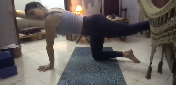 Ompractice teacher Jane Cargill sitting in floral dress in Suhkasana Easy Pose on bed