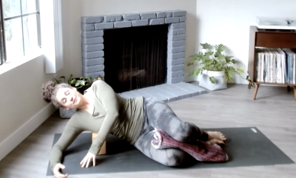 Ompractice teacher Niki Saccareccia lying on side on mat with a blanket and block