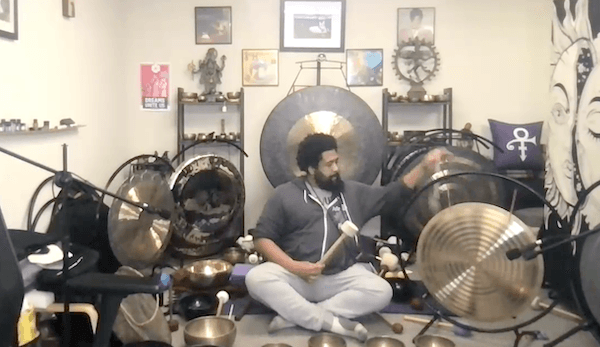 Ompractice teacher Reggie Hubbard in purple shirt sitting on couch with sound bowls