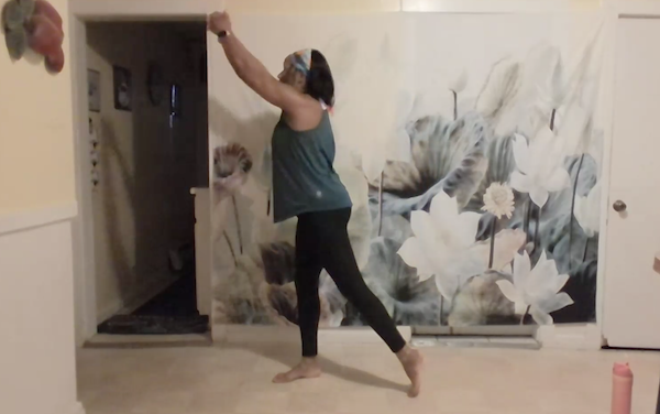 Ompractice teacher Charisse demonstrates a standing pose extending her arms up in the air in a twist