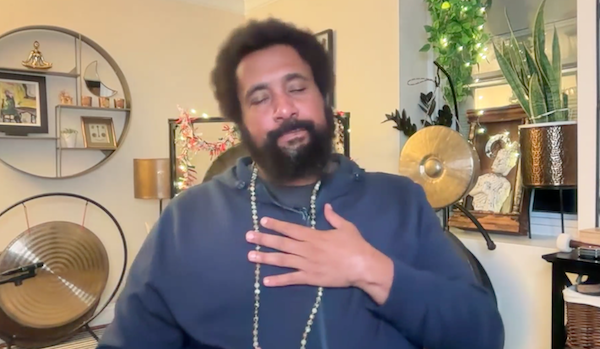 Ompractice teacher Reggie Hubbard in purple shirt sitting on couch with sound bowls