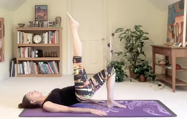 Ompractice Teacher Jayne Schmitz on mat doing a pilates move with leg in the air