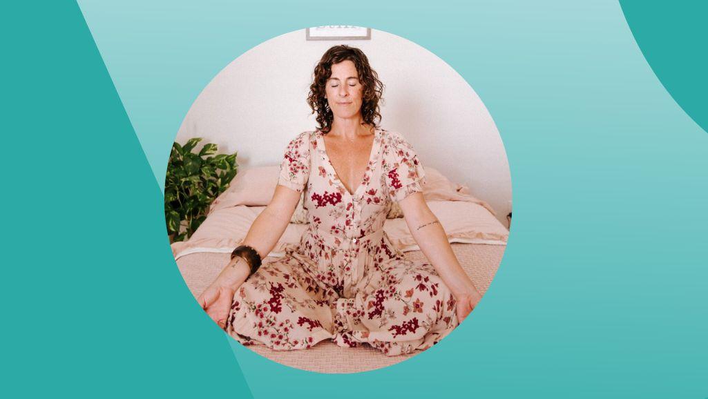 Ompractice teacher Jane Cargill sitting in floral dress in Suhkasana Easy Pose on bed