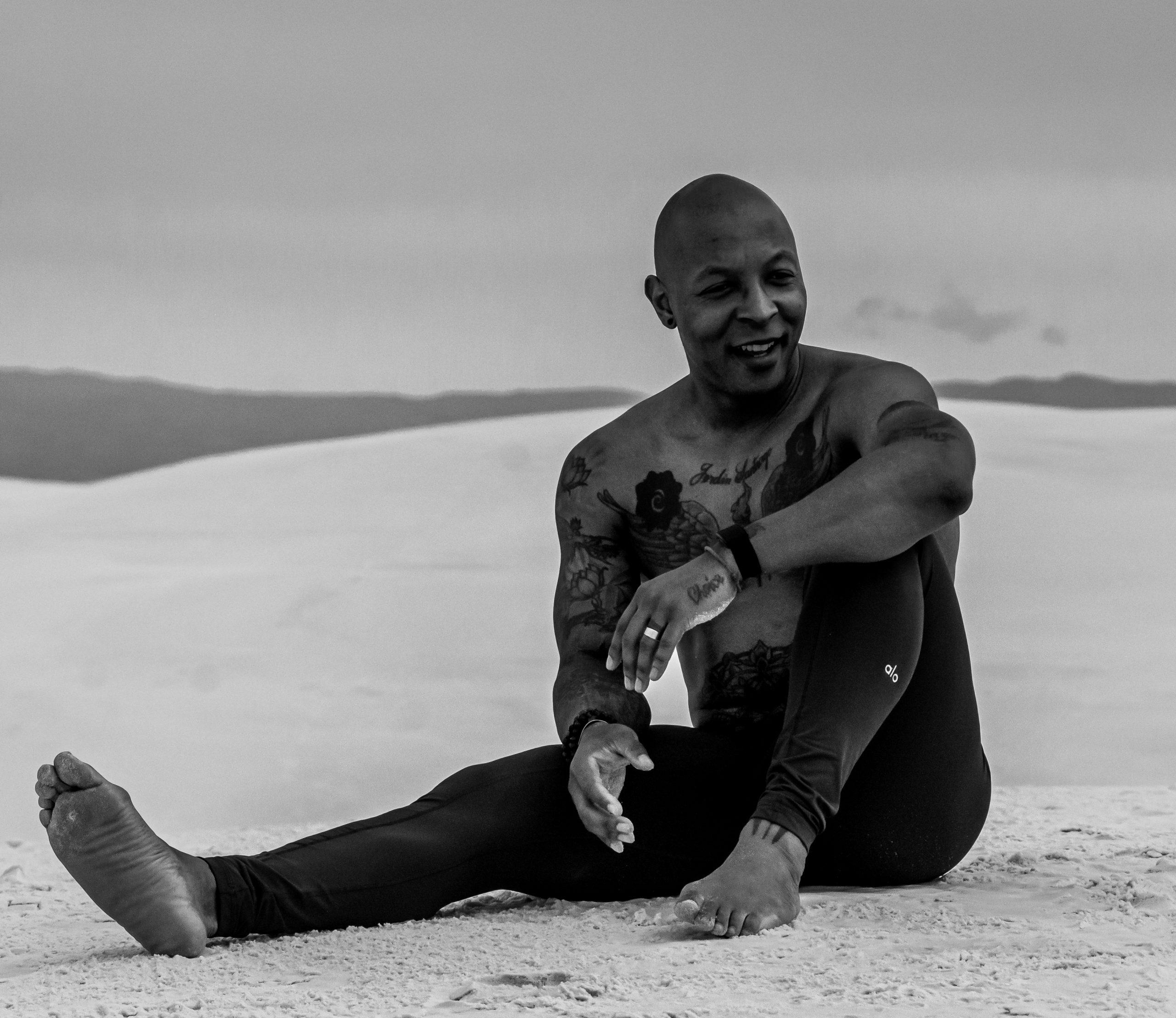 Ompractice teacher Dominic Stanley sitting on sand in black and white