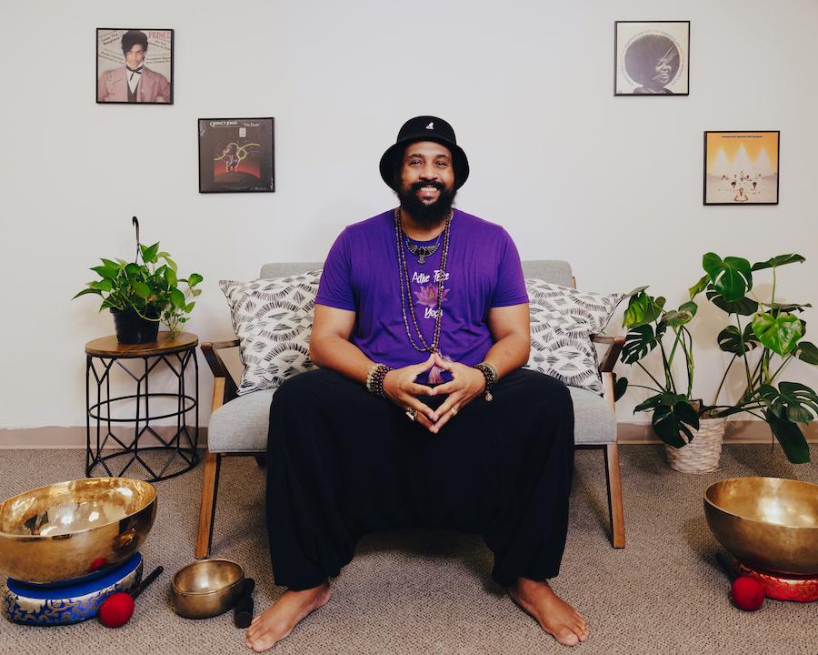 Ompractice teacher Reggie Hubbard in purple shirt sitting on couch with sound bowls