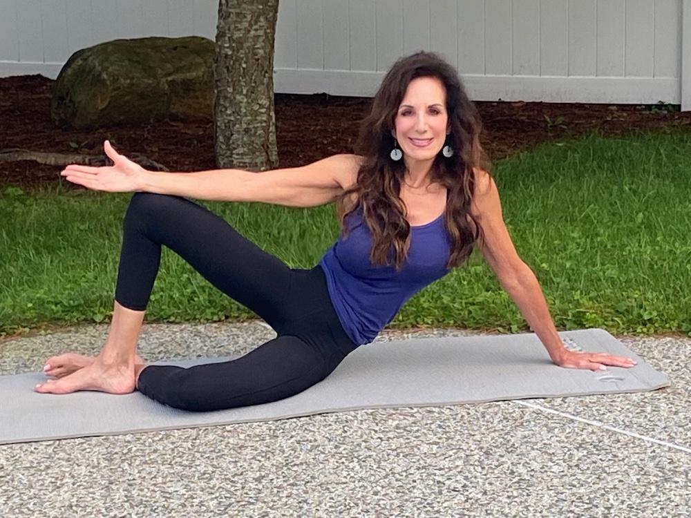 Ompractice teacher Barbara Hospod sitting on Pilates mat in front of grassy area with tree and rock