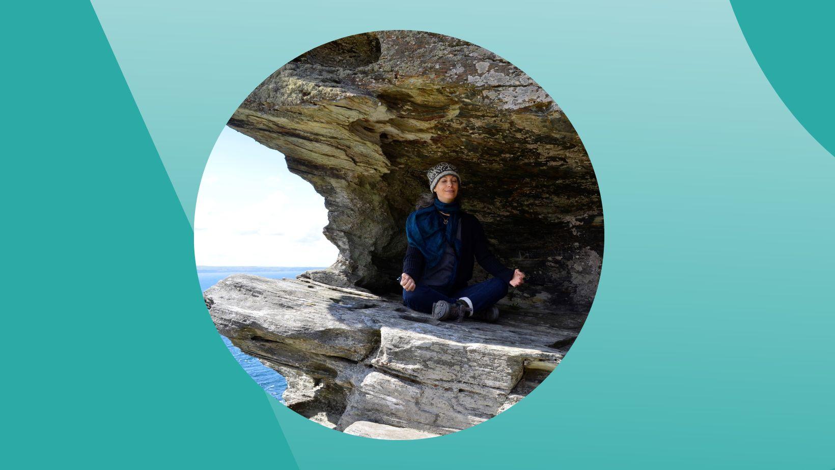 Ompractice teacher Beth Ciesco seated in meditation on a cliff
