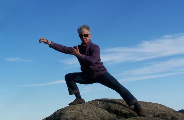 Gurney Bolster, practicing Tai Chi on a boulder with the sky behind her